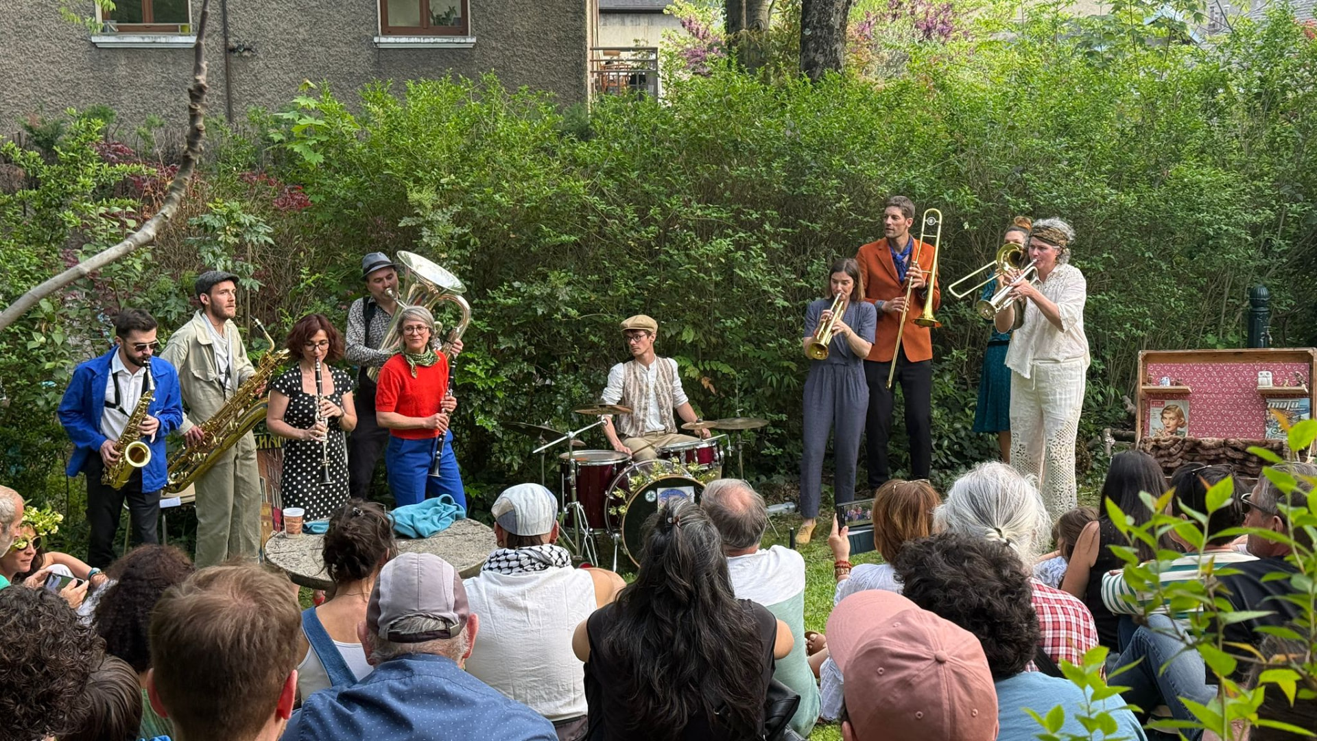 Attico Brass en concert dans un jardin partagé devant un public assis dans l'herbe